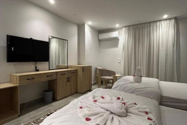 A hotel room with a bed, a desk, a chair, a TV, and a window with curtains.