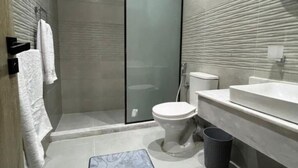 A modern bathroom with a glass shower enclosure, a white toilet, and a large sink. - Triple Room with Garden View at Saloumy Pyramids HotelWonders (Nazlat as Sammān)