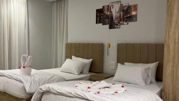 A hotel room with two beds, each with white bedding and pillows, and a wooden headboard. There are towels placed on one bed, and a wall-mounted artwork above the beds. - Triple Room with Garden View at Saloumy Pyramids HotelWonders (Nazlat as Sammān)