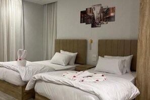 Habitación de hotel con dos camas, cada una con ropa de cama y almohadas blancas, y cabeceros de madera. Hay toallas sobre una cama y una obra de arte colgada en la pared sobre las camas.