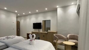 A modern hotel room with two beds, a flat-screen TV, a wooden desk, a chair, and a small round table. - Triple Room with Garden View at Saloumy Pyramids HotelWonders (Nazlat as Sammān)