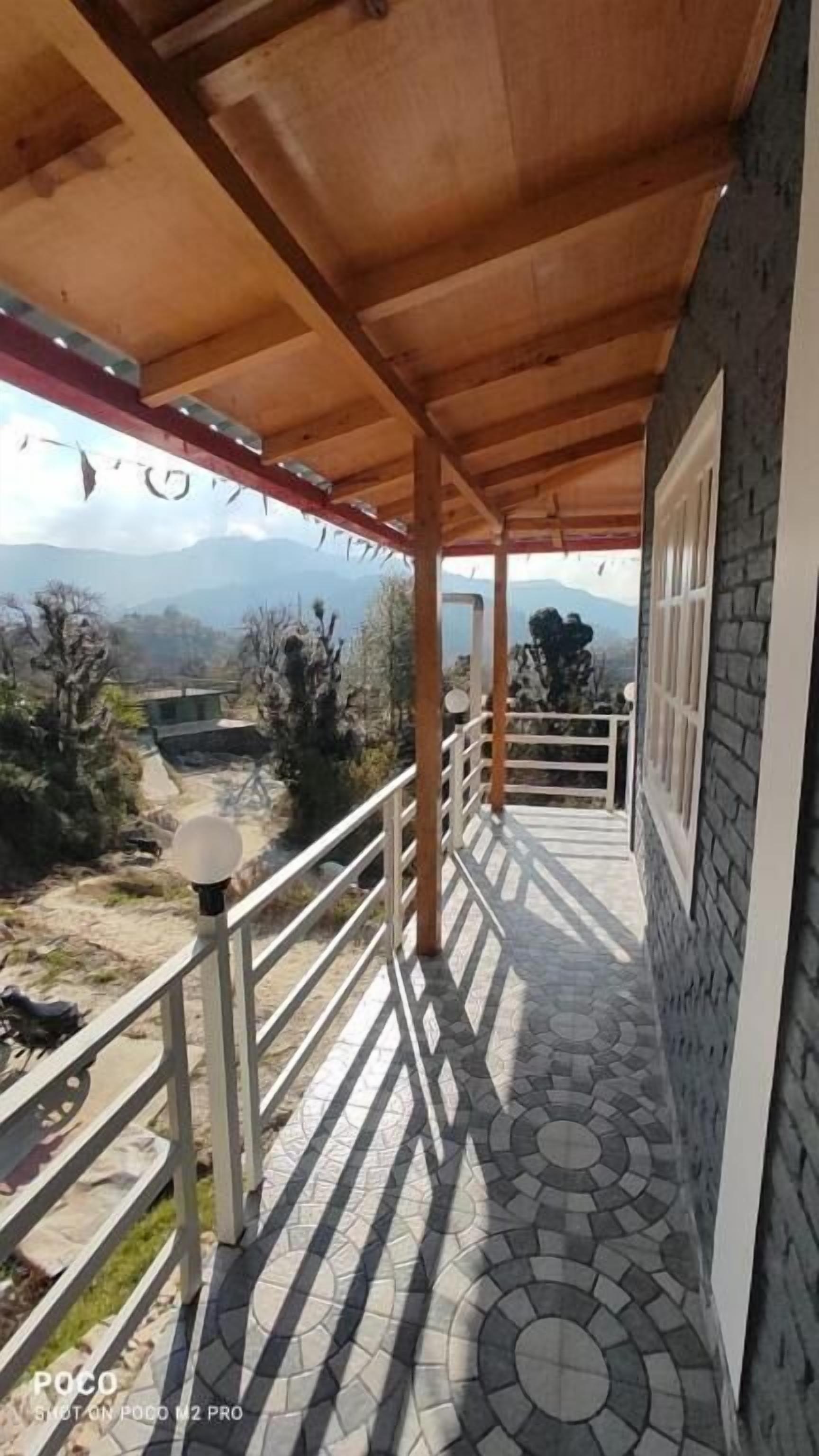 A covered balcony with a tiled floor and a view of the surrounding landscape.