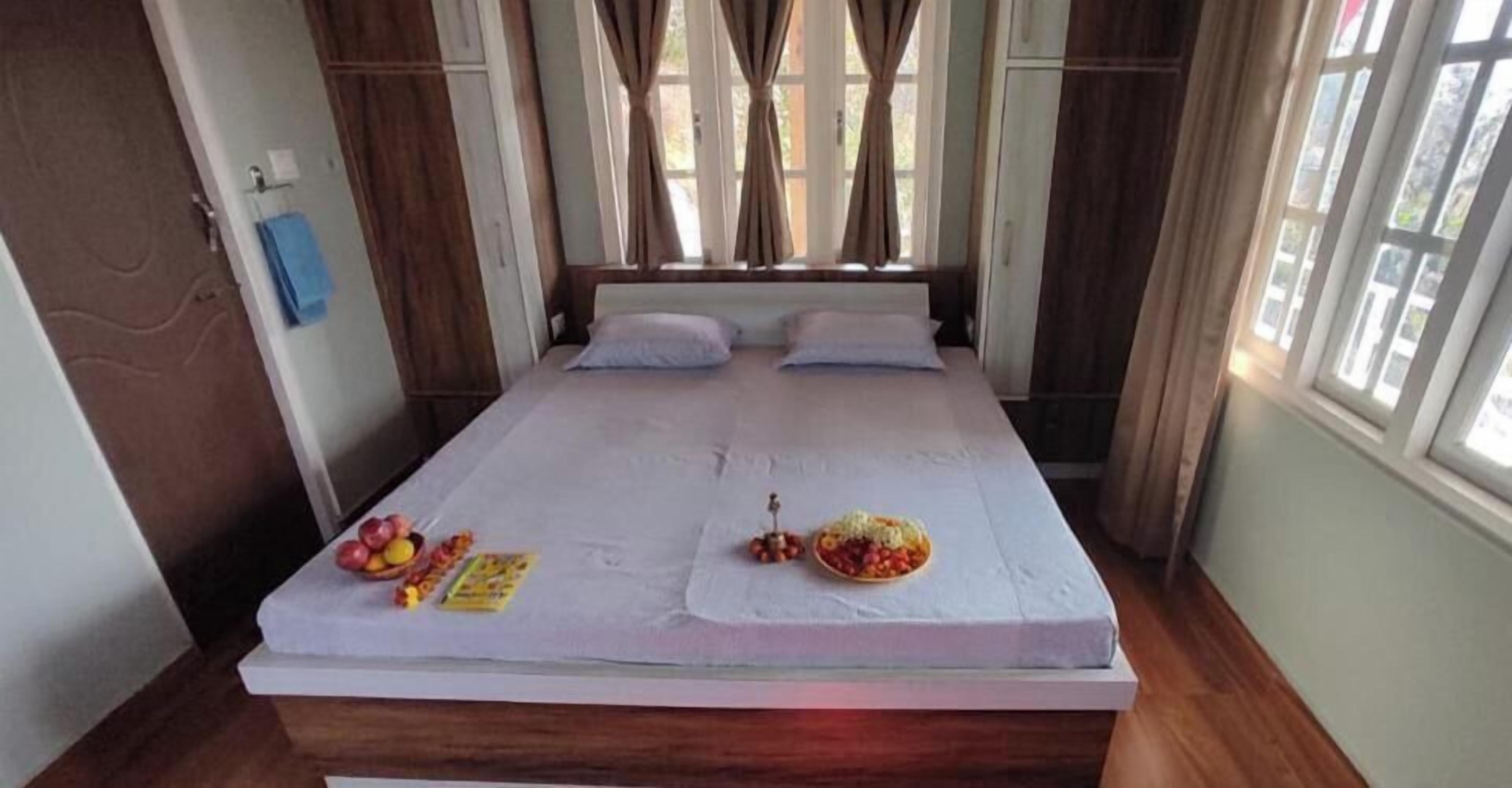 A bed with a white mattress, two pillows, and a small table with fruits and snacks.