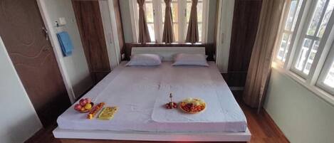 A bed with a white mattress, two pillows, and a small table with fruits and snacks.