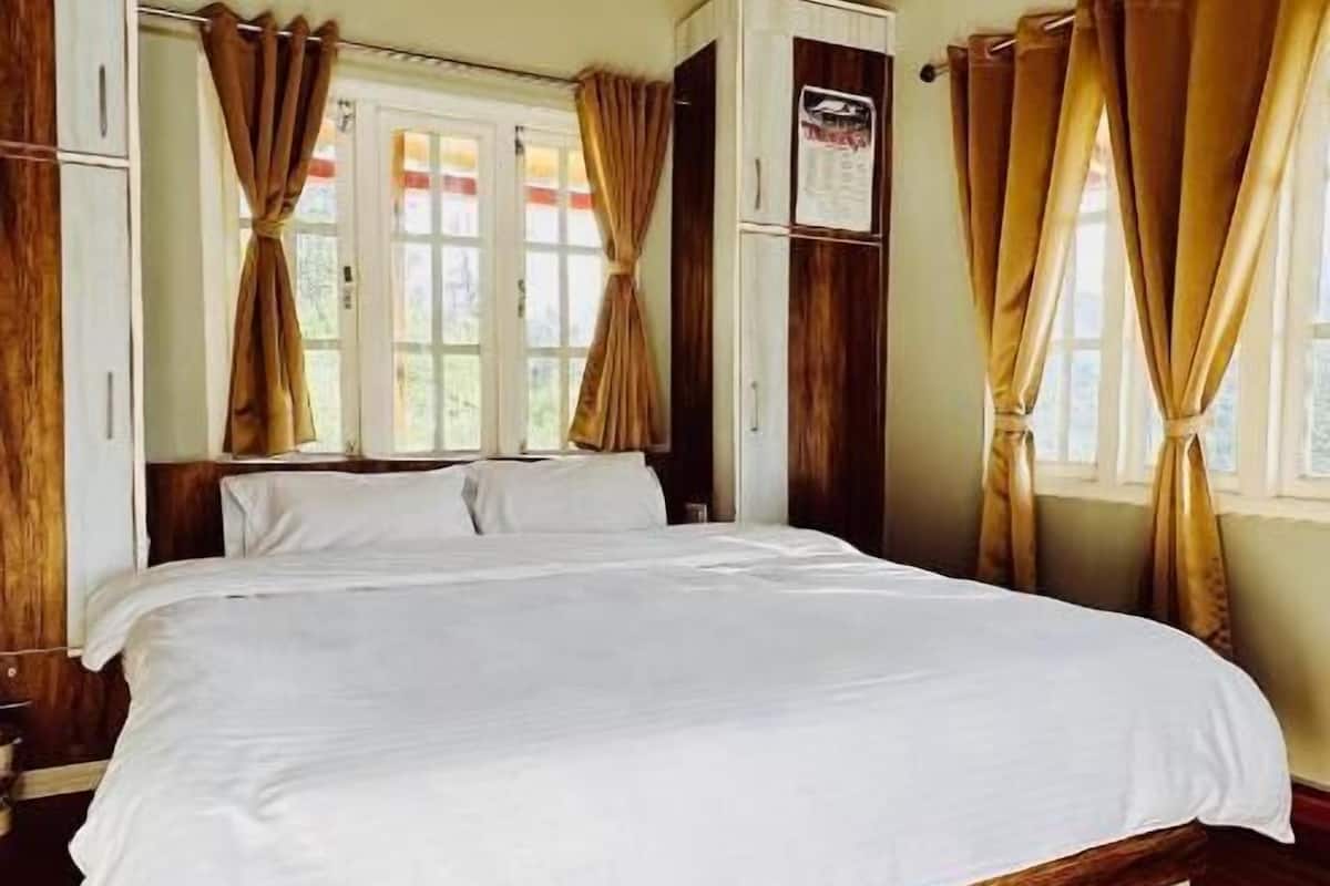 Um quarto com uma cama grande, vigas de madeira no teto, um tapete vermelho e cortinas nas janelas.