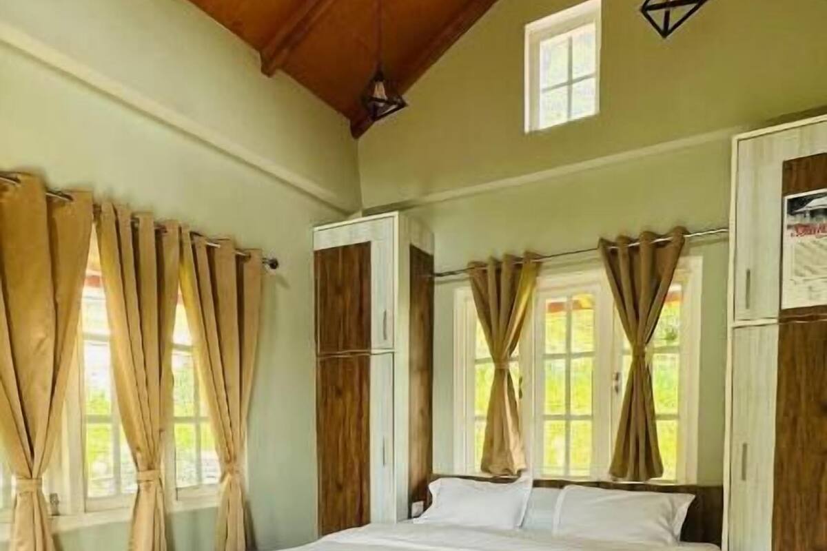 Quarto com teto de madeira, cama com roupa de cama branca, tapete vermelho e cortinas.