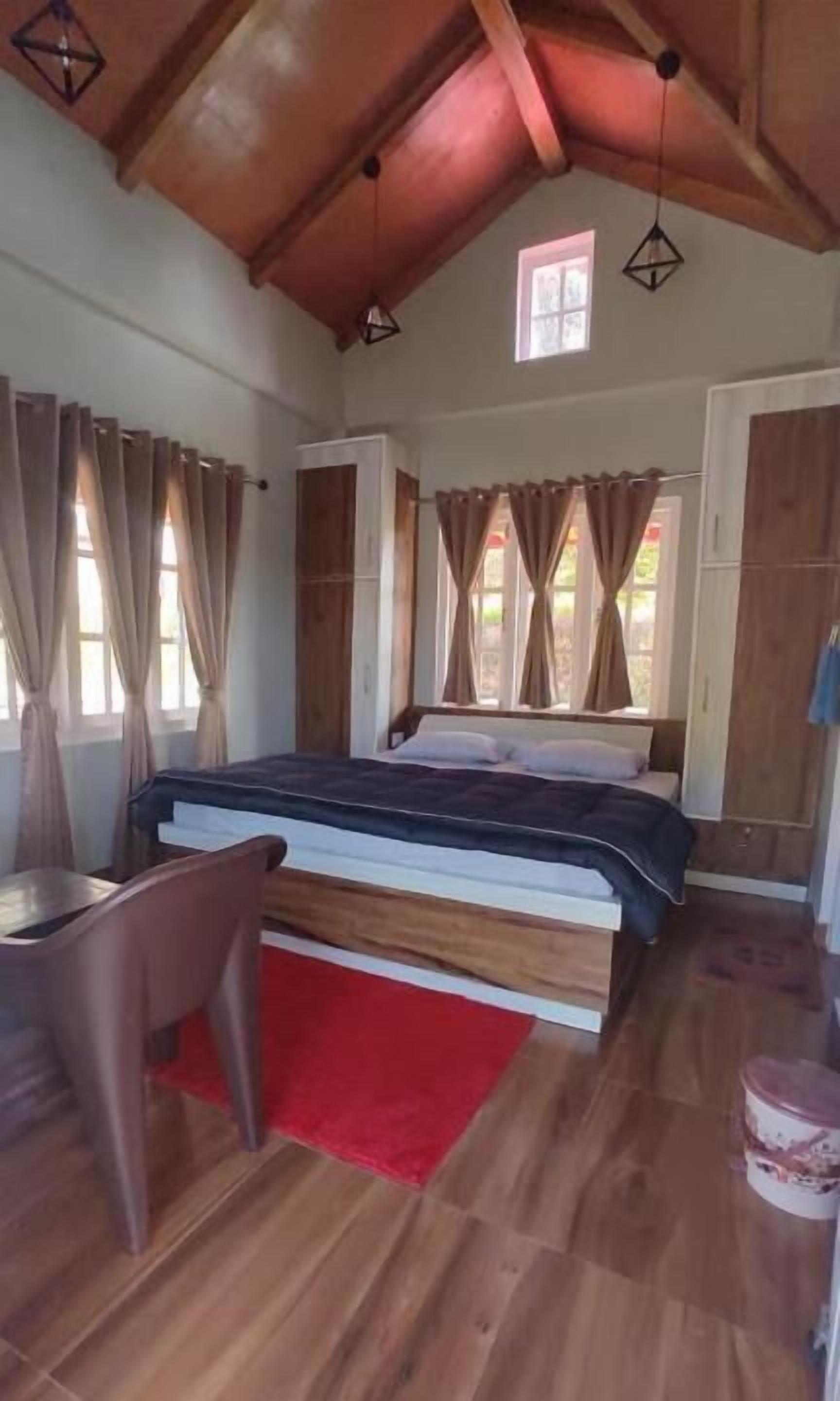 Ein Schlafzimmer mit Bett, Schreibtisch und Stuhl. Vor den Fenstern hängen Vorhänge.