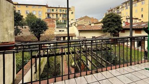 A balcony with a stone lion statue, terracotta roof tiles, and a view of yellow buildings with balconies. - Zanobi 75 in Firenze (Florence)
