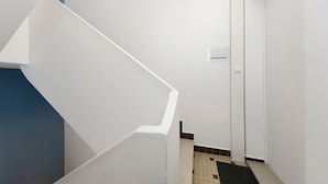 Un intérieur blanc avec un escalier menant à une porte, un sol carrelé et un petit panneau sur le mur.