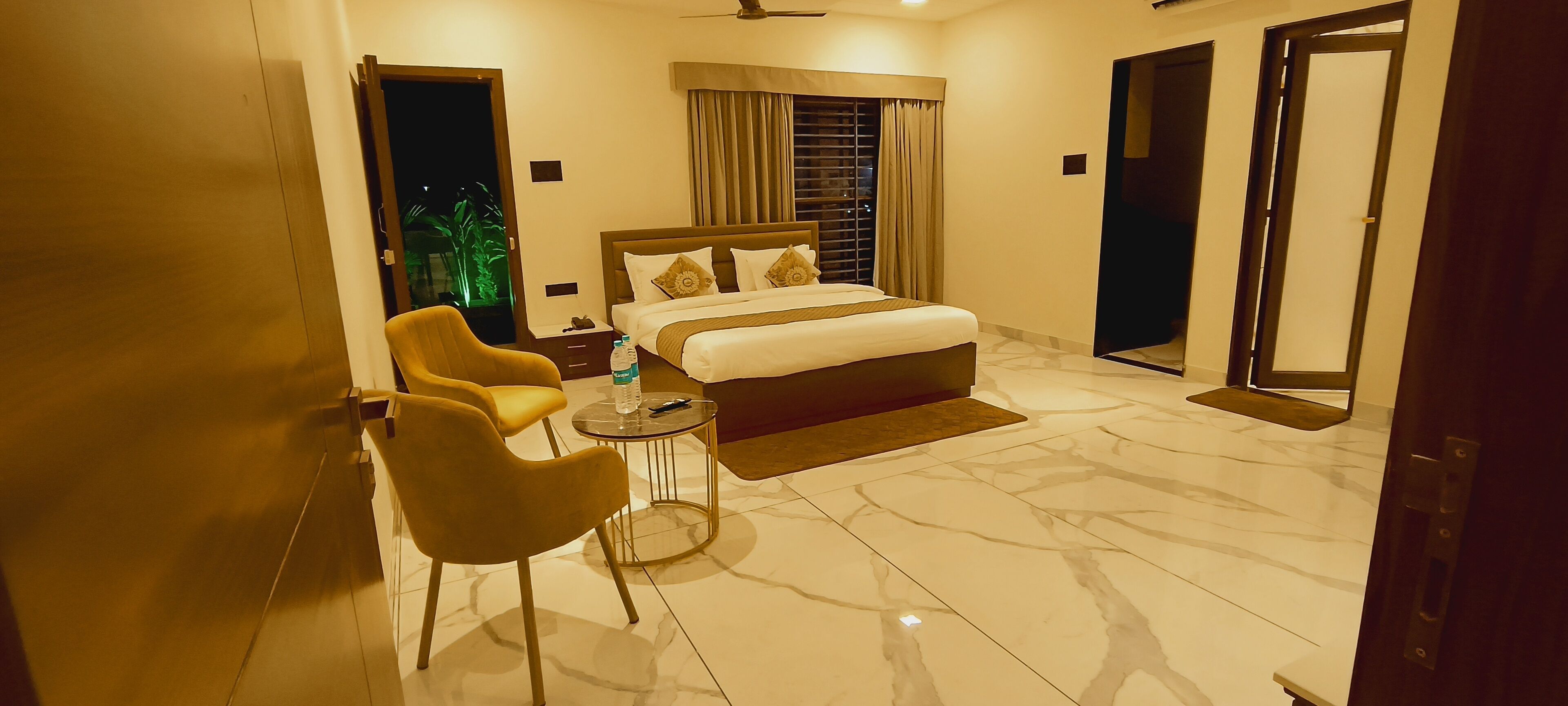 A hotel room with a bed, a chair, a small table, and a mirror.