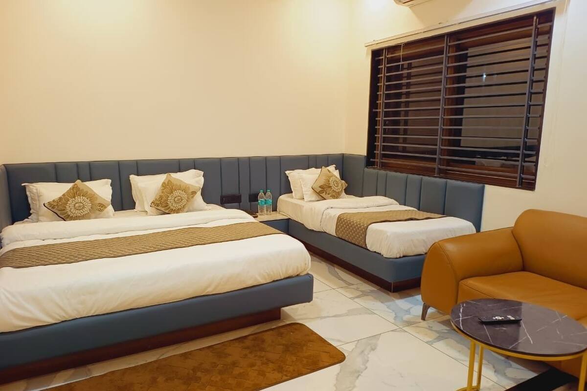 Ein Hotelzimmer mit zwei Betten, einer Couch, einem kleinen Tisch und einem Fenster mit Jalousien.