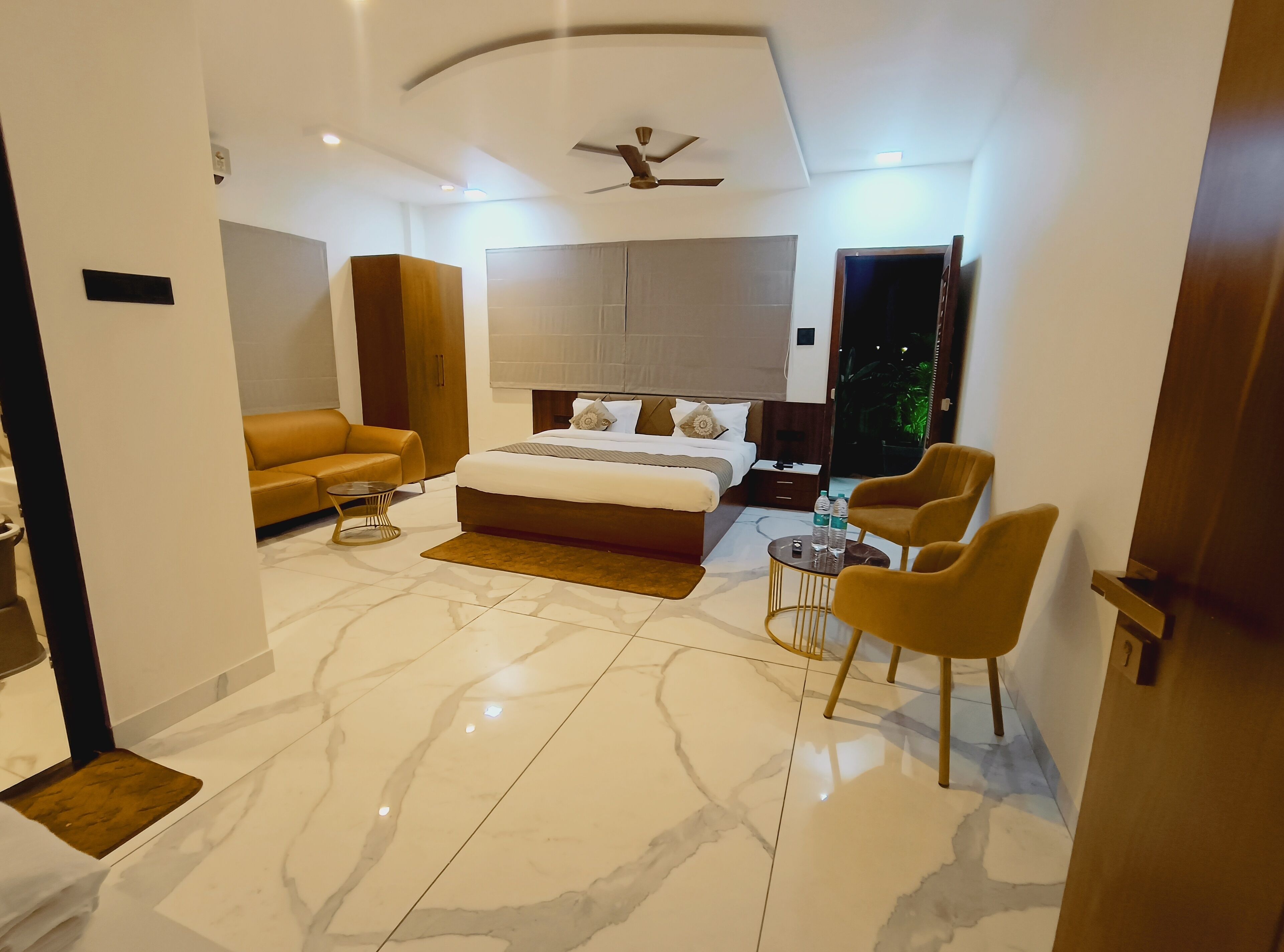 A modern hotel room with a large bed, a sofa, a coffee table, and a seating area with chairs.