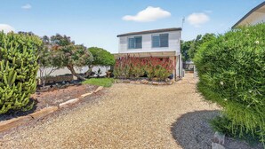Ein modernes, zweistöckiges Haus mit einer Schotterauffahrt, umgeben von verschiedenen Grünpflanzen und einem kleinen Gartenbereich mit roten Blumen.