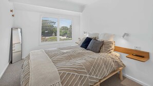 Ein Schlafzimmer mit Bett, Deckenventilator, Fenster mit Jalousien, Nachttisch und Wandleuchte.