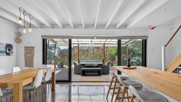 Ein moderner Essbereich mit Holztisch und Stühlen, einer Couch und Blick auf einen Garten durch große Glasfenster.
