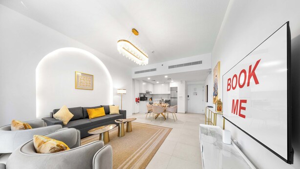 Ein modernes Wohnzimmer mit einer Couch, einem Couchtisch und einem Fernseher. Im Hintergrund ist eine Küche erkennbar.