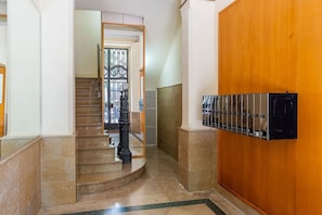 Un pasillo con una puerta de madera, una escalera y un buzón en la pared.