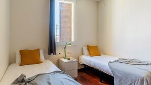 A small, tidy room with two single beds, a nightstand with a lamp, and a window with curtains. - Penthouse with stunning TERRACE / Arco de Triunfo (08009 Barcelona)