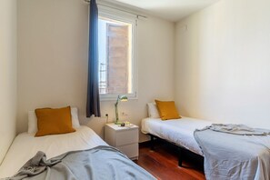 A small, tidy room with two single beds, a nightstand with a lamp, and a window with curtains. - Penthouse with stunning TERRACE / Arco de Triunfo (08009 Barcelona)