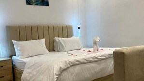A neatly made bed with white linens and a beige headboard, a bedside table with a drawer, and a small vase with a white flower. - Spacious King Room with Mountain View Near the Giza Pyramids (Nazlat as Sammān)