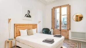 Un dormitorio con cama de madera, una silla, un radiador, una ventana con vistas y un cuadro enmarcado en la pared.