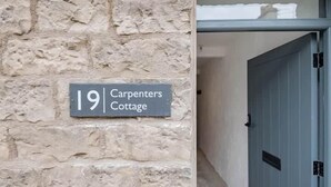 Un mur de pierres sur lequel est apposée une plaque indiquant : « 19, Cottage des charpentiers ».