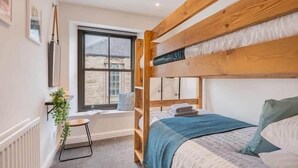 Une chambre avec un lit superposé, une petite fenêtre, un radiateur et une plante.