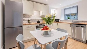 Une cuisine moderne avec des meubles blancs, un réfrigérateur en acier inoxydable et une table à manger avec des chaises.