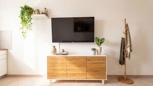 A modern living room with a flat-screen TV mounted on the wall, a wooden cabinet with decorative items, a plant, and a coat rack. - Apollo Apartment (Palermo)