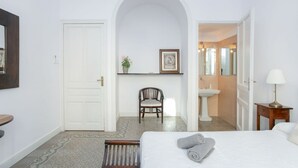 Een hotelkamer met een bed, een stoel, een klein tafeltje, een wastafel en een spiegel.