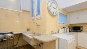 Een kleine keuken met een spoelbak, fornuis, magnetron en een klok aan de muur.