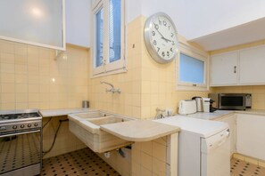 Eine kleine Küche mit Spüle, Herd, Mikrowelle und einer Wanduhr.