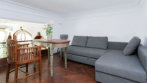 Een kamer met een grijze bank, een houten stoel, een ronde tafel en een potplant.