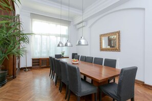 Une salle à manger avec une table en bois, des chaises à revêtement gris, des luminaires suspendus, un grand miroir et une plante en pot.