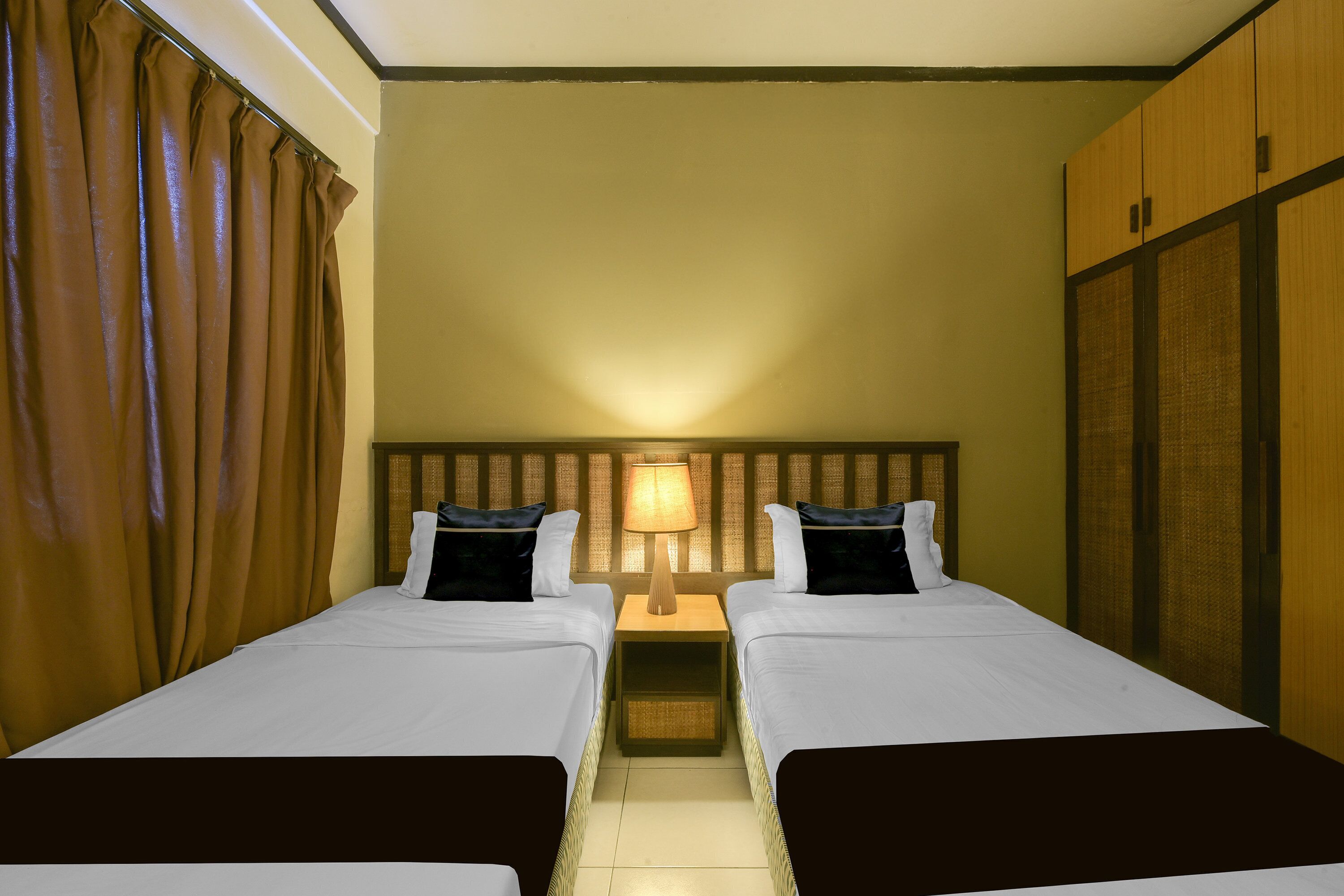 A hotel room with two beds, a nightstand with a lamp, and a wardrobe.