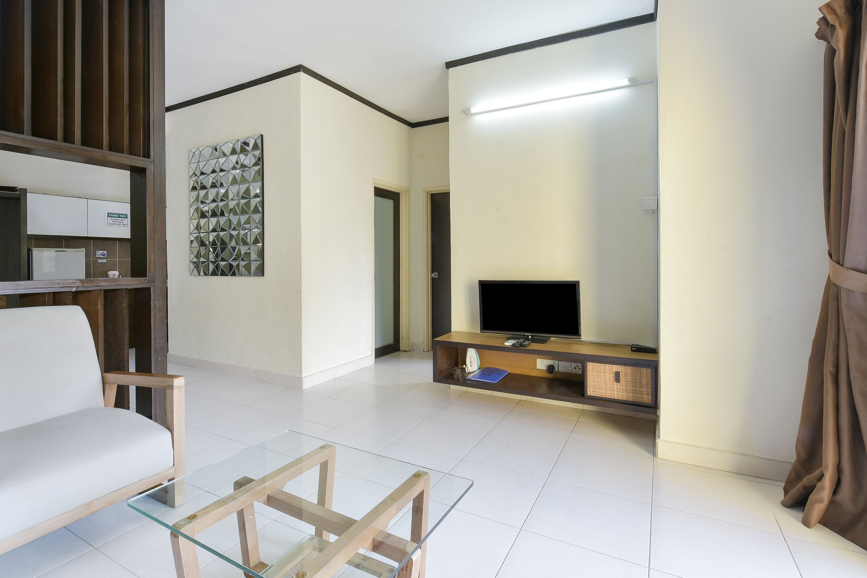 A modern living room with a glass coffee table, a white sofa, a flat-screen TV on a wooden stand, and a wall-mounted mirror.