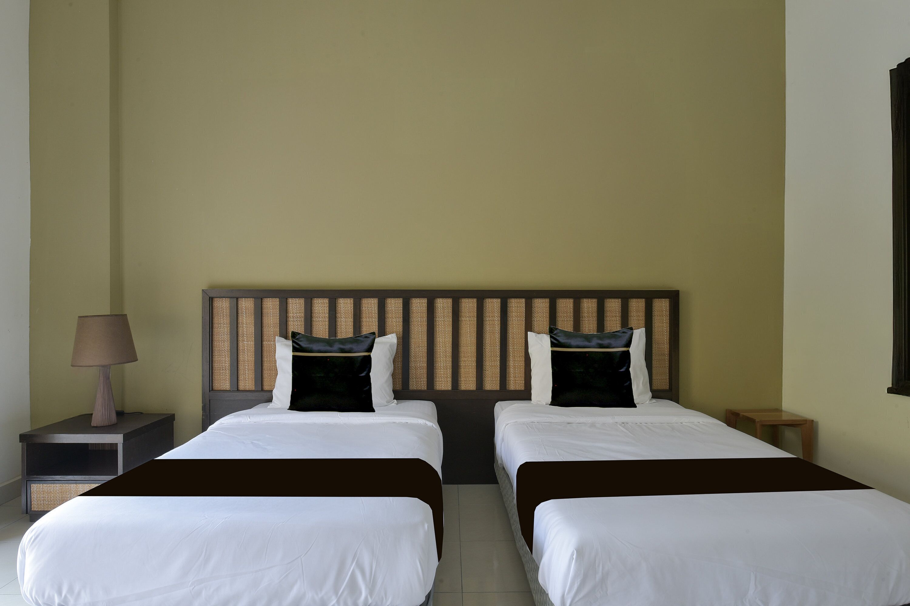Habitación de hotel con dos camas, una mesita de noche con lámpara, una pequeña mesa y una ventana.