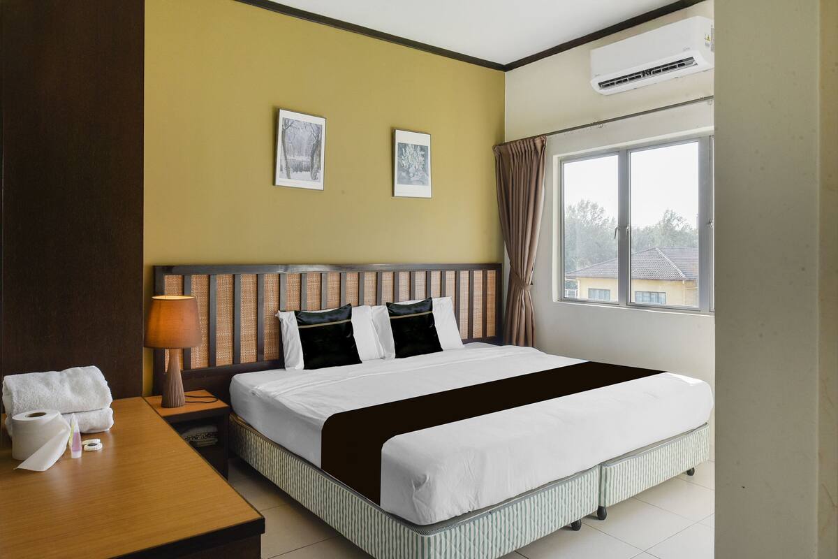 A hotel room with a bed, a nightstand, a lamp, a window with curtains, and two framed pictures on the wall.