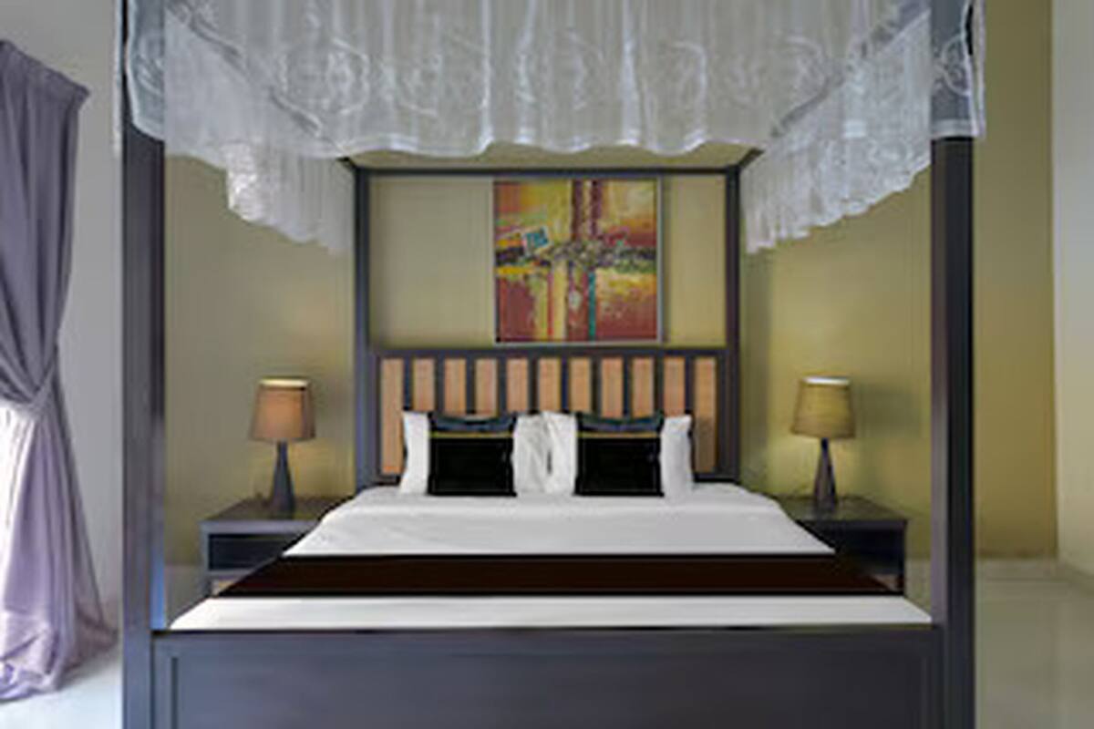 A four-poster bed with a lace canopy, a painting above the headboard, and two bedside lamps.