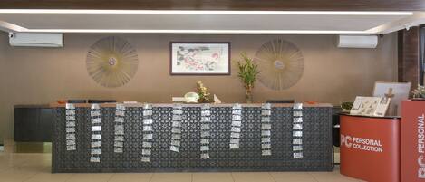 A reception desk with a patterned backdrop, framed artwork, and a red 'PERSONAL COLLECTION' counter.