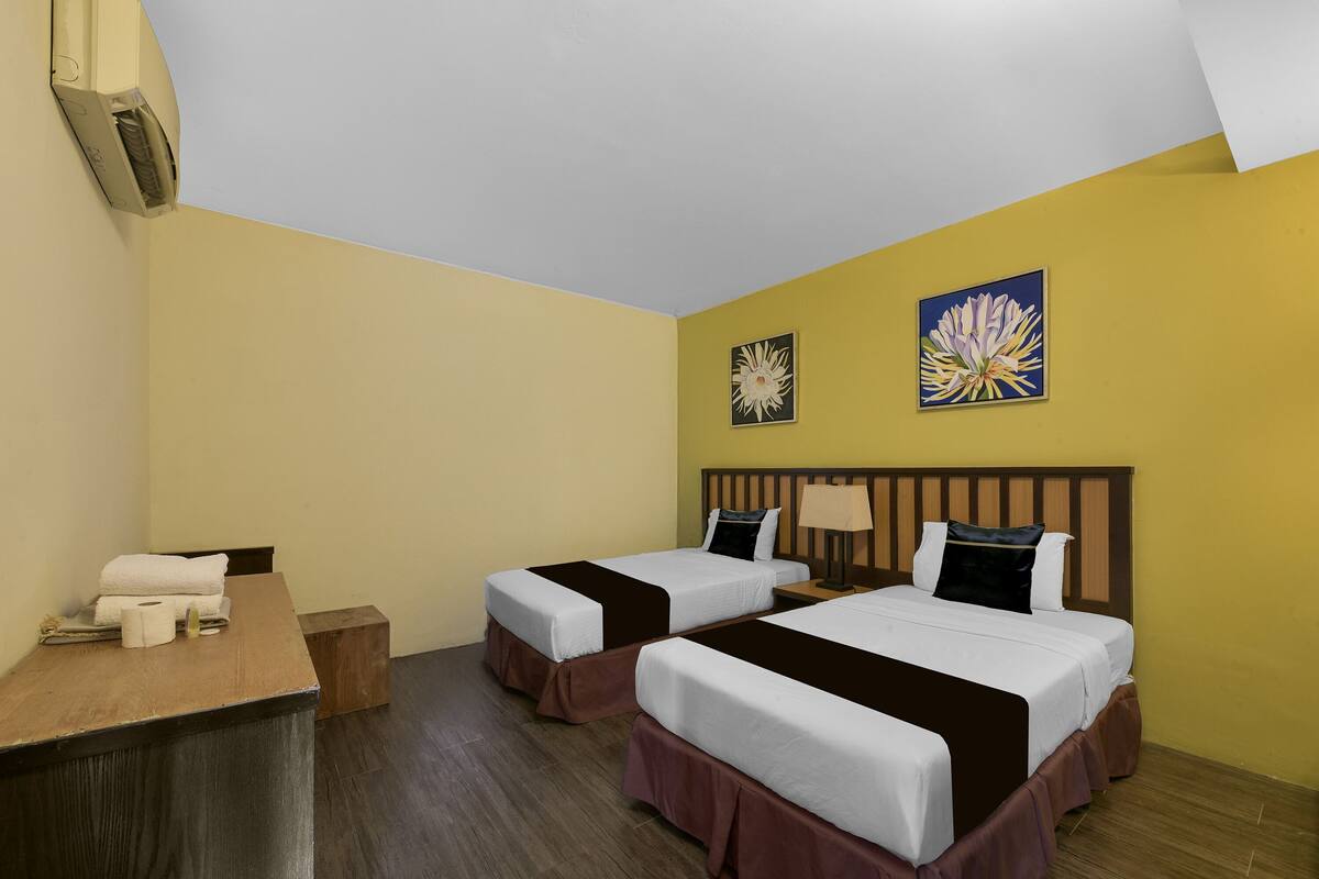 A hotel room with two beds, a desk, and two wall-mounted paintings.