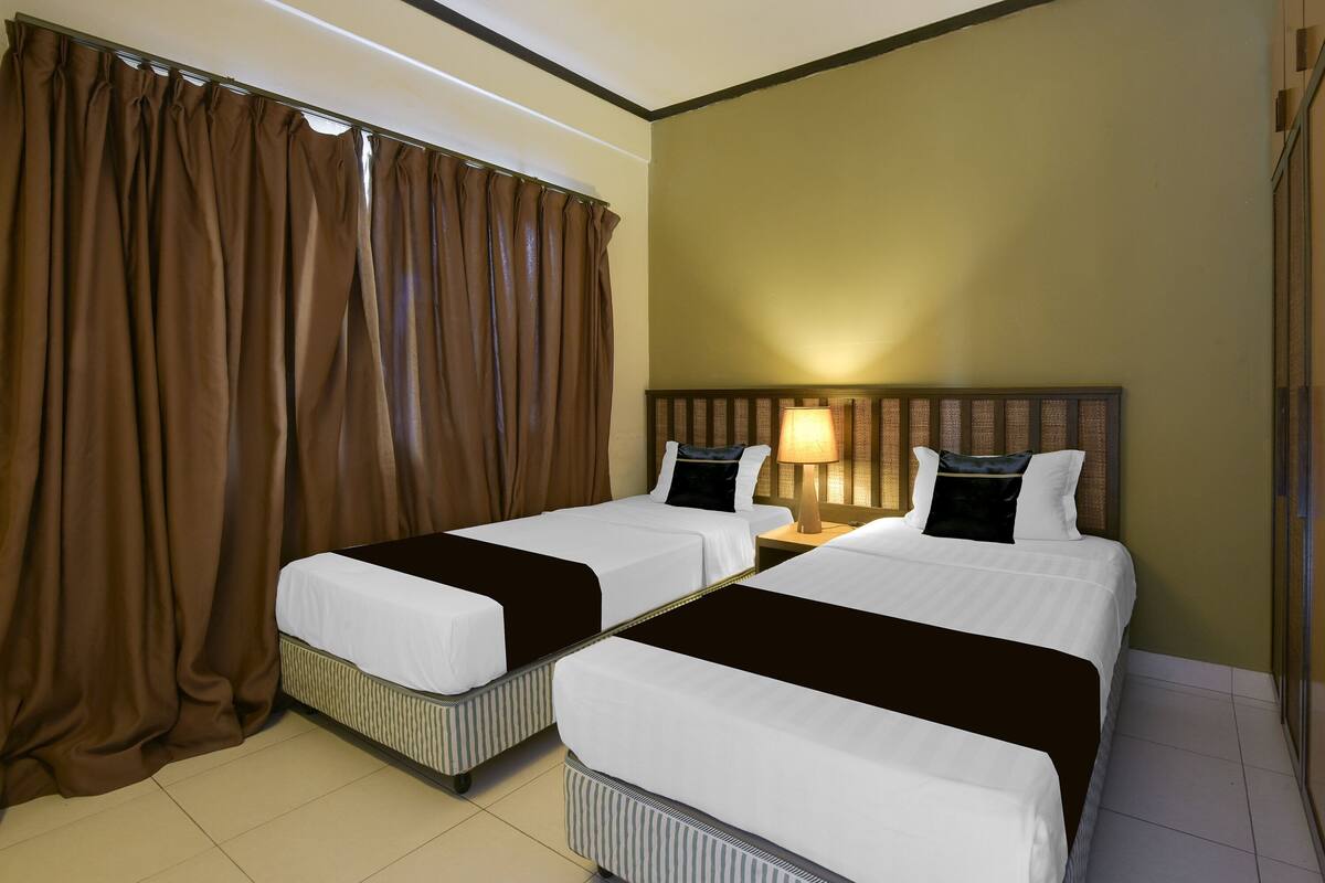 A hotel room with two single beds, a nightstand with a lamp, and a large window with curtains.