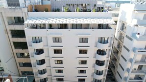 Un edificio de varios pisos con balcones, ventanas amplias y una terraza en la azotea con sombrillas.