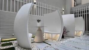 Un espacio interior moderno con asientos blancos y curvos alrededor de una mesa central, rodeado por una valla blanca y un suelo con diseño.