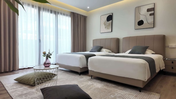 Una habitación de hotel con dos camas, una mesita con un florero y arte abstracto en la pared.