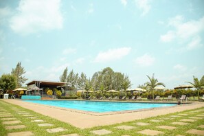 A swimming pool with lounge chairs and umbrellas, surrounded by trees and a building with a covered area.