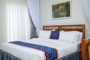 A neatly made bed with a patterned bedspread, a framed picture on the wall, and a window with sheer curtains.