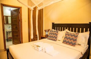 A neatly made bed with white linens and two decorative pillows, a wooden headboard, and a bedside table with a vase.
