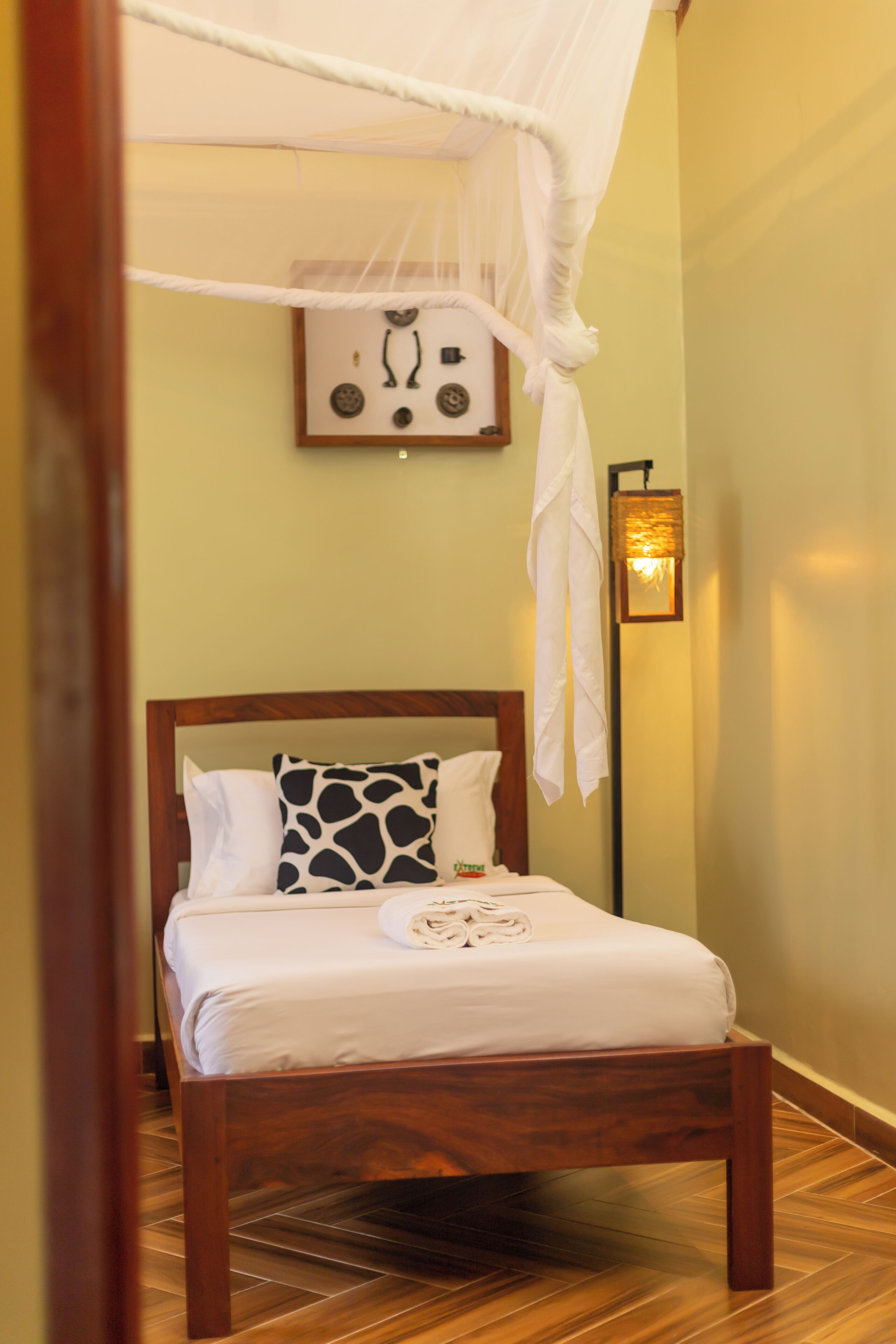 A neatly made bed with a canopy, a framed picture on the wall, and a floor lamp.