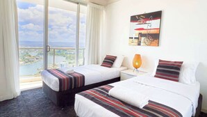 Quarto de hotel com duas camas, uma janela grande com vista para a cidade e uma luminária no teto.